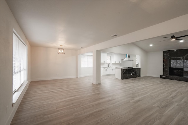 unfurnished living room with ceiling fan, lofted ceiling, a premium fireplace, and light hardwood / wood-style flooring