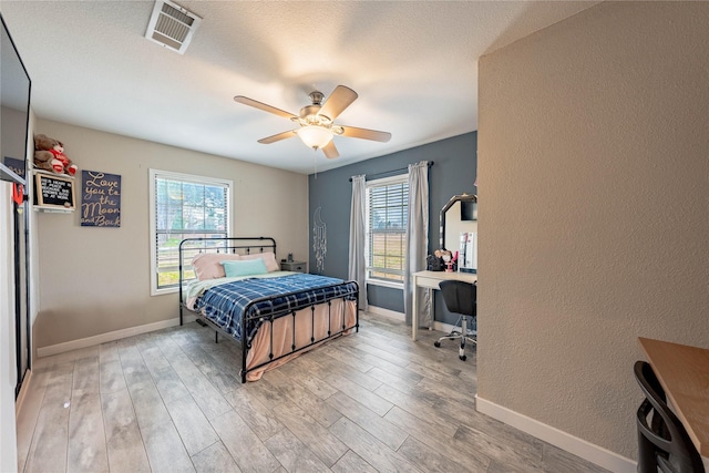 bedroom featuring multiple windows, a textured ceiling, light hardwood / wood-style flooring, and ceiling fan