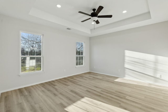 spare room with light hardwood / wood-style flooring, a raised ceiling, and ceiling fan