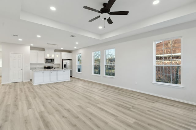 unfurnished living room featuring ceiling fan, light wood-type flooring, and a tray ceiling