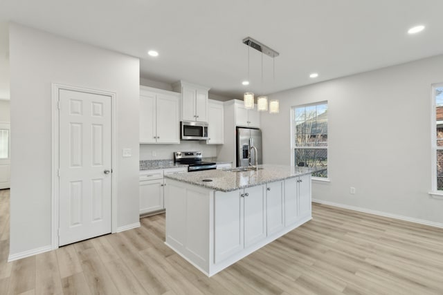 kitchen featuring decorative light fixtures, an island with sink, white cabinets, stainless steel appliances, and light stone countertops