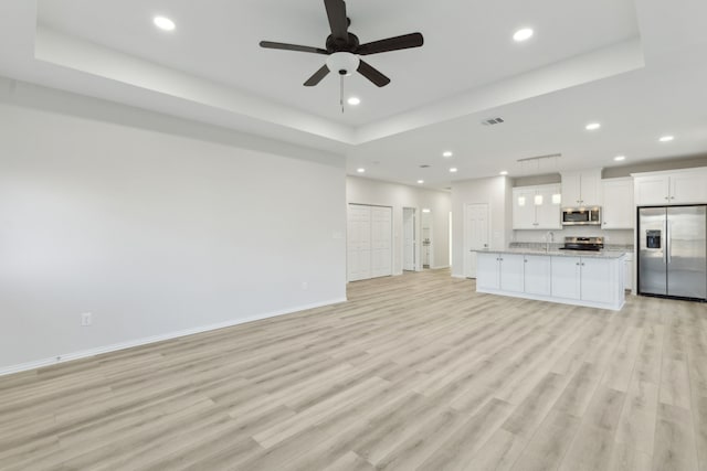 unfurnished living room with ceiling fan, a raised ceiling, sink, and light hardwood / wood-style flooring