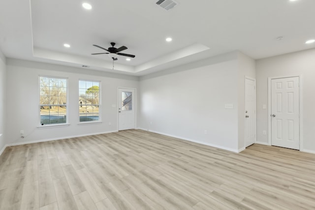 unfurnished living room with ceiling fan, a tray ceiling, and light hardwood / wood-style floors