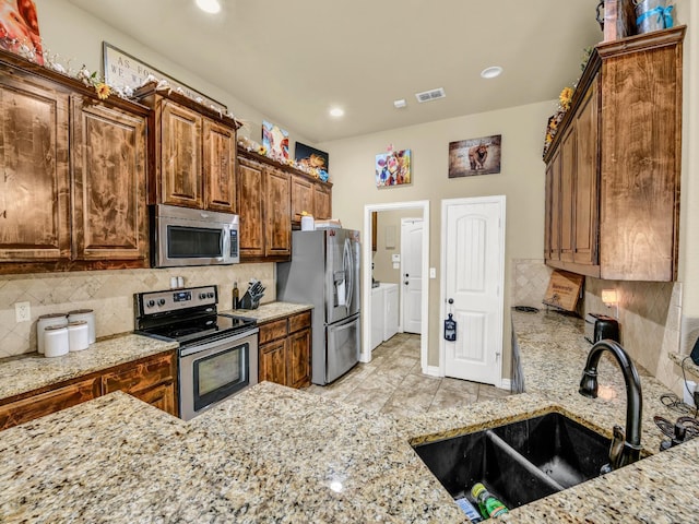 kitchen with sink, light stone counters, washer and dryer, stainless steel appliances, and backsplash