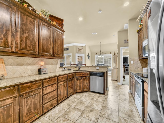 kitchen with pendant lighting, sink, stainless steel appliances, light stone countertops, and kitchen peninsula