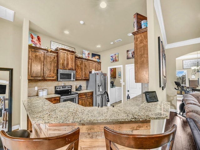 kitchen featuring appliances with stainless steel finishes, light stone counters, tasteful backsplash, separate washer and dryer, and kitchen peninsula