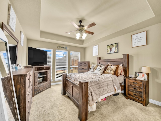 bedroom with light colored carpet, ceiling fan, and a tray ceiling