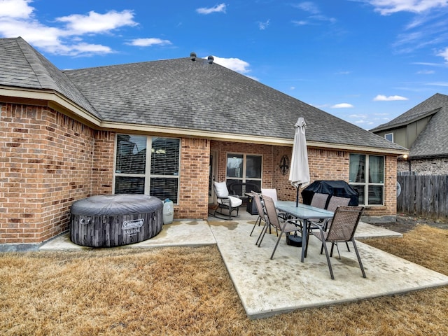 rear view of house featuring a hot tub, a patio, and a lawn