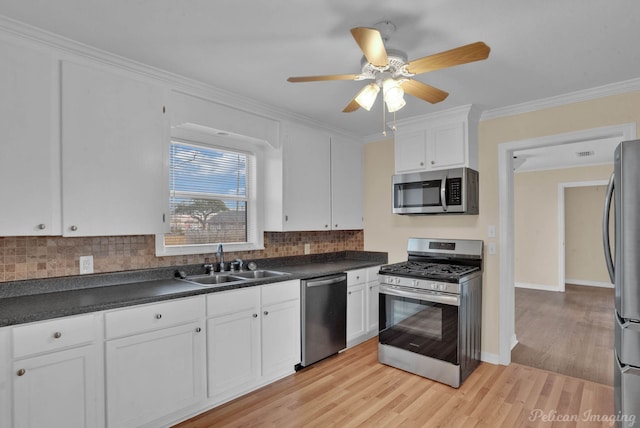 kitchen featuring a sink, white cabinetry, appliances with stainless steel finishes, dark countertops, and crown molding