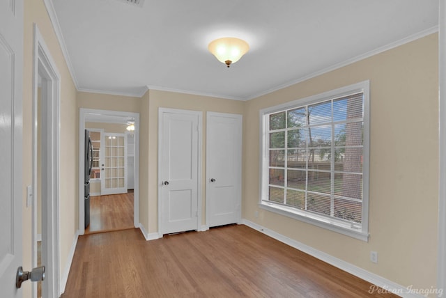 unfurnished bedroom featuring light wood-style floors, freestanding refrigerator, ornamental molding, and baseboards