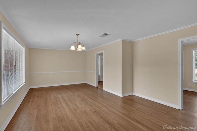 spare room featuring wood finished floors, visible vents, baseboards, ornamental molding, and an inviting chandelier