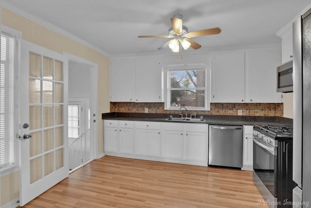 kitchen featuring a sink, white cabinets, appliances with stainless steel finishes, light wood finished floors, and dark countertops