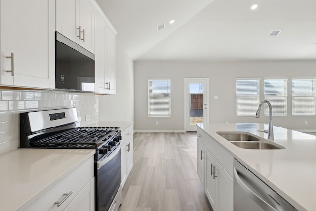 kitchen with sink, appliances with stainless steel finishes, white cabinets, decorative backsplash, and vaulted ceiling