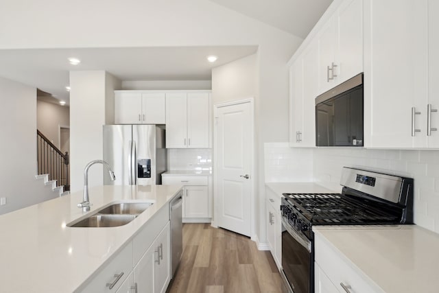 kitchen featuring white cabinetry, sink, backsplash, stainless steel appliances, and light hardwood / wood-style flooring