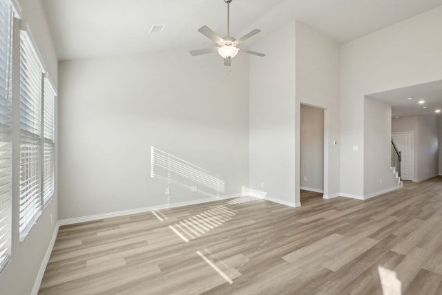 empty room with light hardwood / wood-style flooring, a towering ceiling, and plenty of natural light