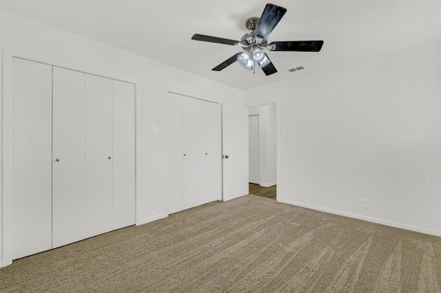 unfurnished bedroom featuring ceiling fan, carpet floors, and multiple closets