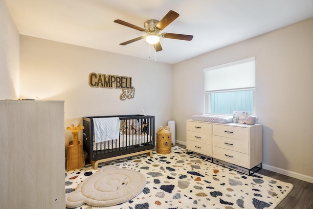 bedroom featuring dark wood-type flooring, a crib, and ceiling fan