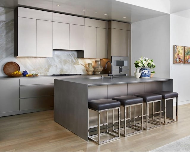 kitchen with sink, gas cooktop, a kitchen breakfast bar, and light hardwood / wood-style flooring