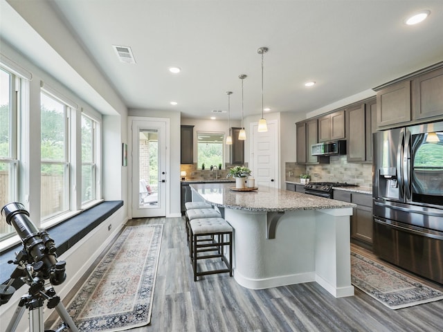 kitchen with a kitchen island, appliances with stainless steel finishes, sink, hanging light fixtures, and light stone counters