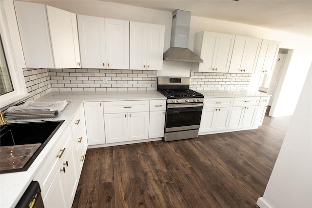 kitchen featuring dark wood-type flooring, wall chimney exhaust hood, stainless steel range with gas cooktop, and white cabinets