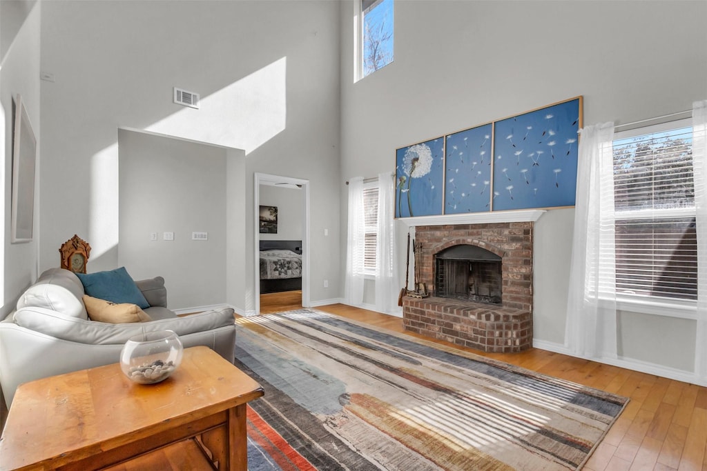 living room with a brick fireplace, hardwood / wood-style flooring, and a high ceiling