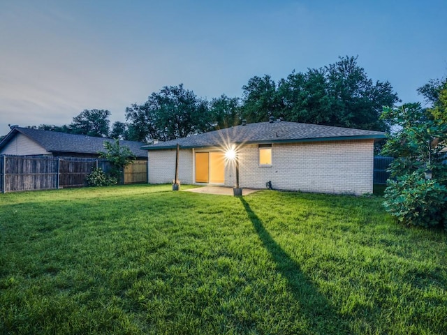 rear view of house featuring a fenced backyard, a yard, and brick siding