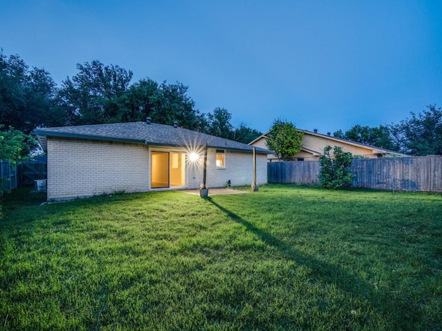 rear view of house featuring a fenced backyard, a yard, and brick siding