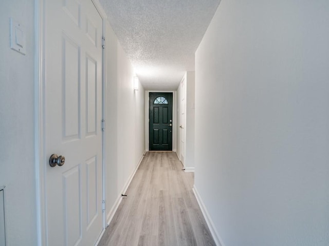 hallway featuring a textured ceiling, baseboards, and light wood-style floors