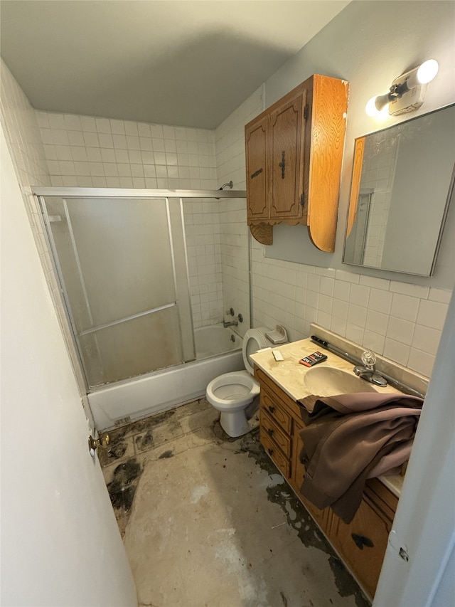 full bathroom with tile walls, bath / shower combo with glass door, vanity, concrete floors, and toilet