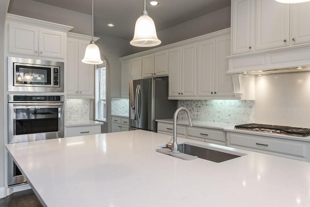 kitchen featuring appliances with stainless steel finishes, sink, white cabinets, and decorative light fixtures