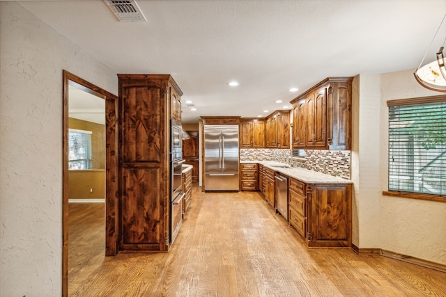 kitchen featuring built in appliances, backsplash, light hardwood / wood-style floors, and sink