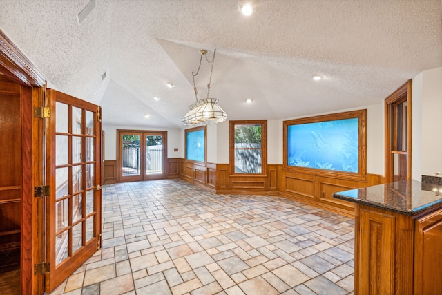 interior space with vaulted ceiling, pendant lighting, dark stone counters, a textured ceiling, and french doors