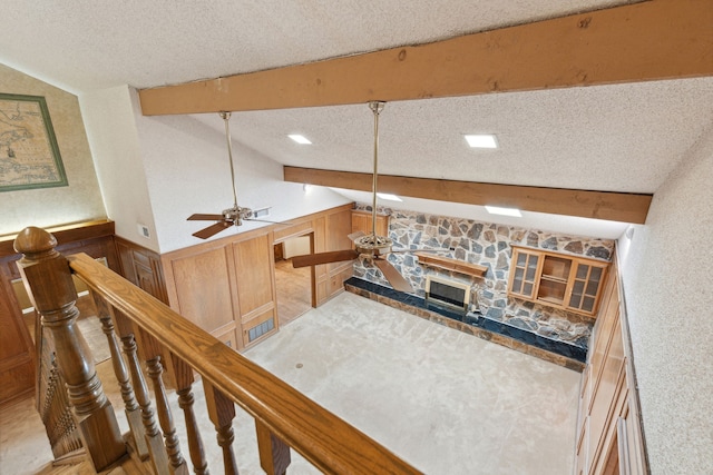 living room with lofted ceiling with beams, ceiling fan, a stone fireplace, and a textured ceiling