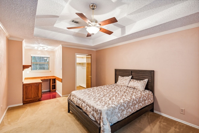 carpeted bedroom with built in desk, ceiling fan, a tray ceiling, crown molding, and a textured ceiling