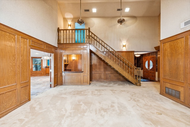 unfurnished living room featuring wood walls, light carpet, and a high ceiling