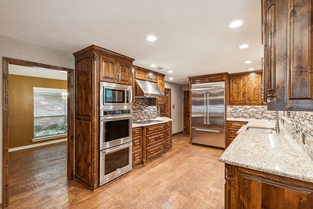 kitchen featuring sink, light hardwood / wood-style flooring, range hood, built in appliances, and light stone counters