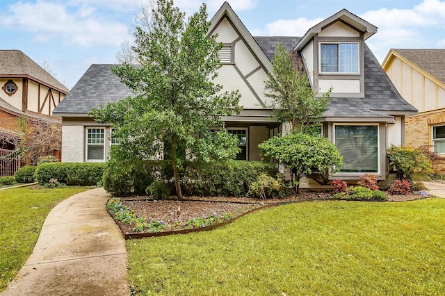 tudor home with stucco siding, a shingled roof, a front lawn, and brick siding