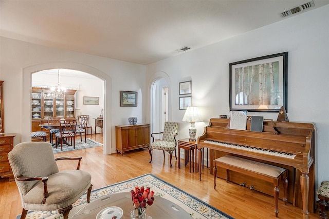 living area featuring light wood finished floors, visible vents, arched walkways, and an inviting chandelier