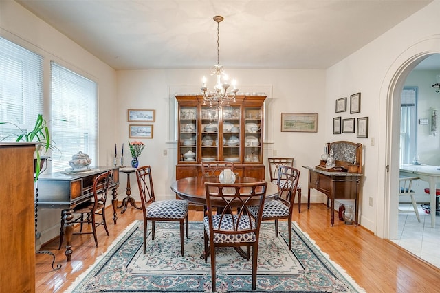 dining space with a chandelier, arched walkways, light wood-style flooring, and baseboards