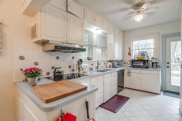 kitchen with tasteful backsplash, under cabinet range hood, light countertops, black appliances, and a sink