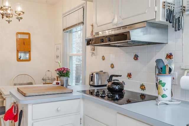 kitchen with decorative backsplash, a peninsula, black electric stovetop, light countertops, and under cabinet range hood