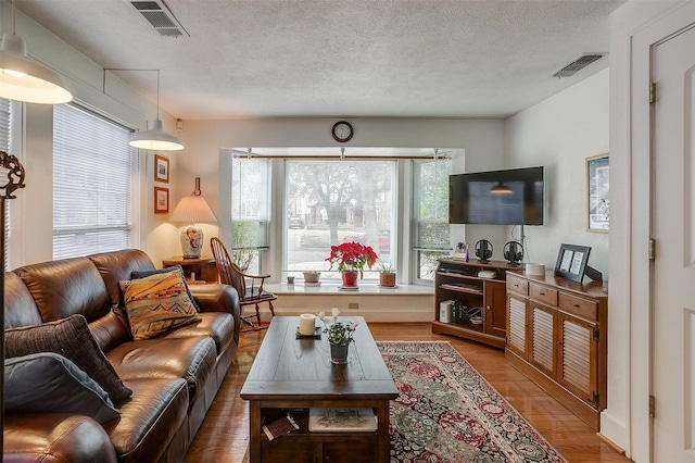 living room featuring a textured ceiling, light wood finished floors, and visible vents