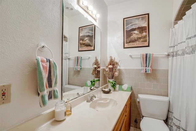 bathroom featuring a wainscoted wall, vanity, toilet, and tile walls