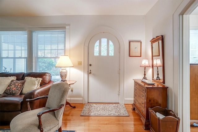 entrance foyer with arched walkways, baseboards, and light wood finished floors