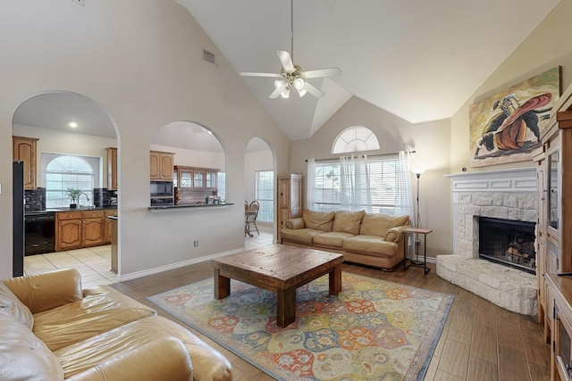 living room with ceiling fan, high vaulted ceiling, a fireplace, and light hardwood / wood-style flooring