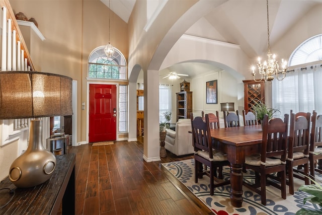 dining space with a wealth of natural light, dark wood-type flooring, high vaulted ceiling, and ceiling fan with notable chandelier