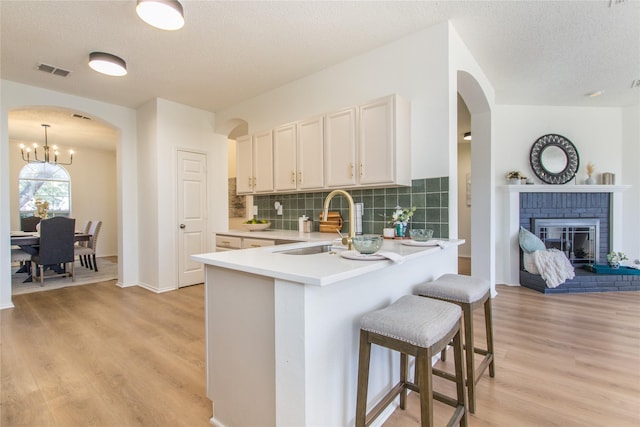 kitchen with pendant lighting, sink, light hardwood / wood-style floors, a brick fireplace, and decorative backsplash