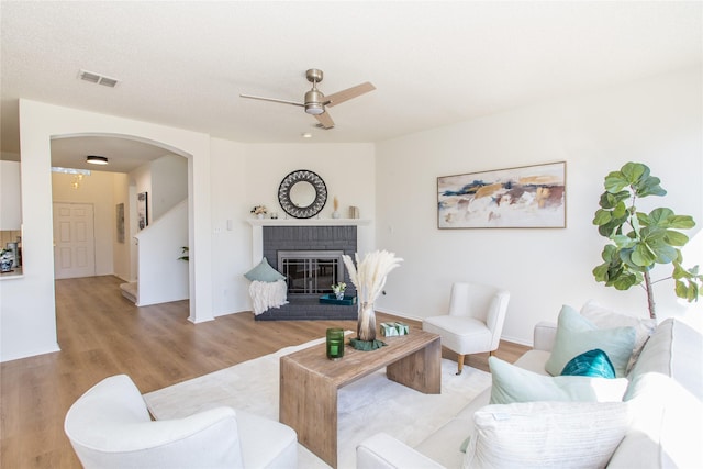 living room with a brick fireplace, ceiling fan, and light hardwood / wood-style flooring