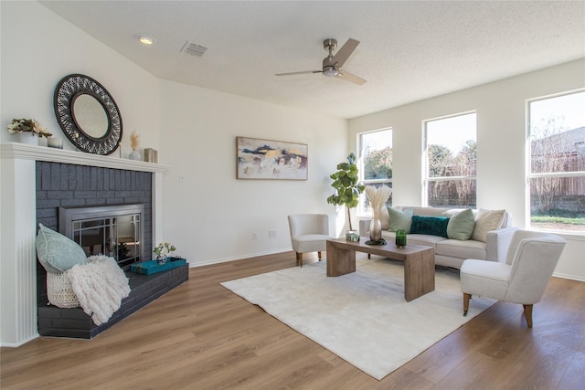 living room featuring a brick fireplace, a healthy amount of sunlight, hardwood / wood-style floors, and a textured ceiling