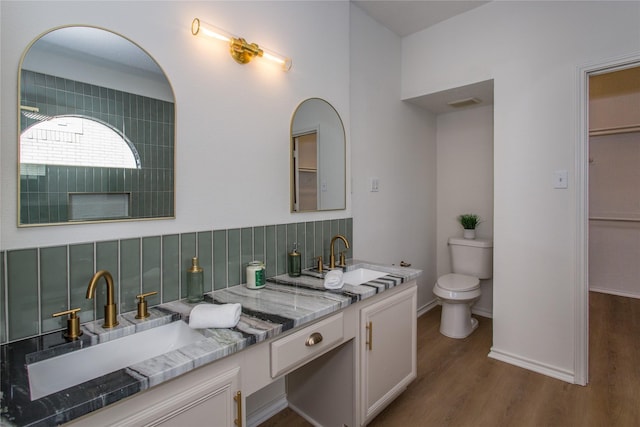 bathroom featuring wood-type flooring, toilet, vanity, and decorative backsplash